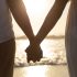 Mid section of couple standing together hand in hand on the beach